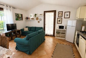 A living room with a sofa, TV, and kitchen area with a fridge and microwave. - Villa Fiammetta, 500 meters from the beach (Castiadas)