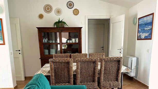 A living room with a teal sofa, wicker chairs, a wooden cabinet, and a dining table. - Villa Fiammetta, 500 meters from the beach (Castiadas)