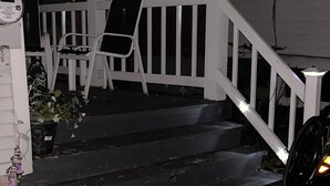 Eine Treppe aus schwarzen Steinen führt zu einer Veranda mit weißen Geländern und einem weißen Stuhl.
