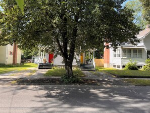 A residential street with houses, a tree, and a sidewalk.