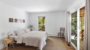 A bedroom with a bed, bedside table, chair, window, and artwork.