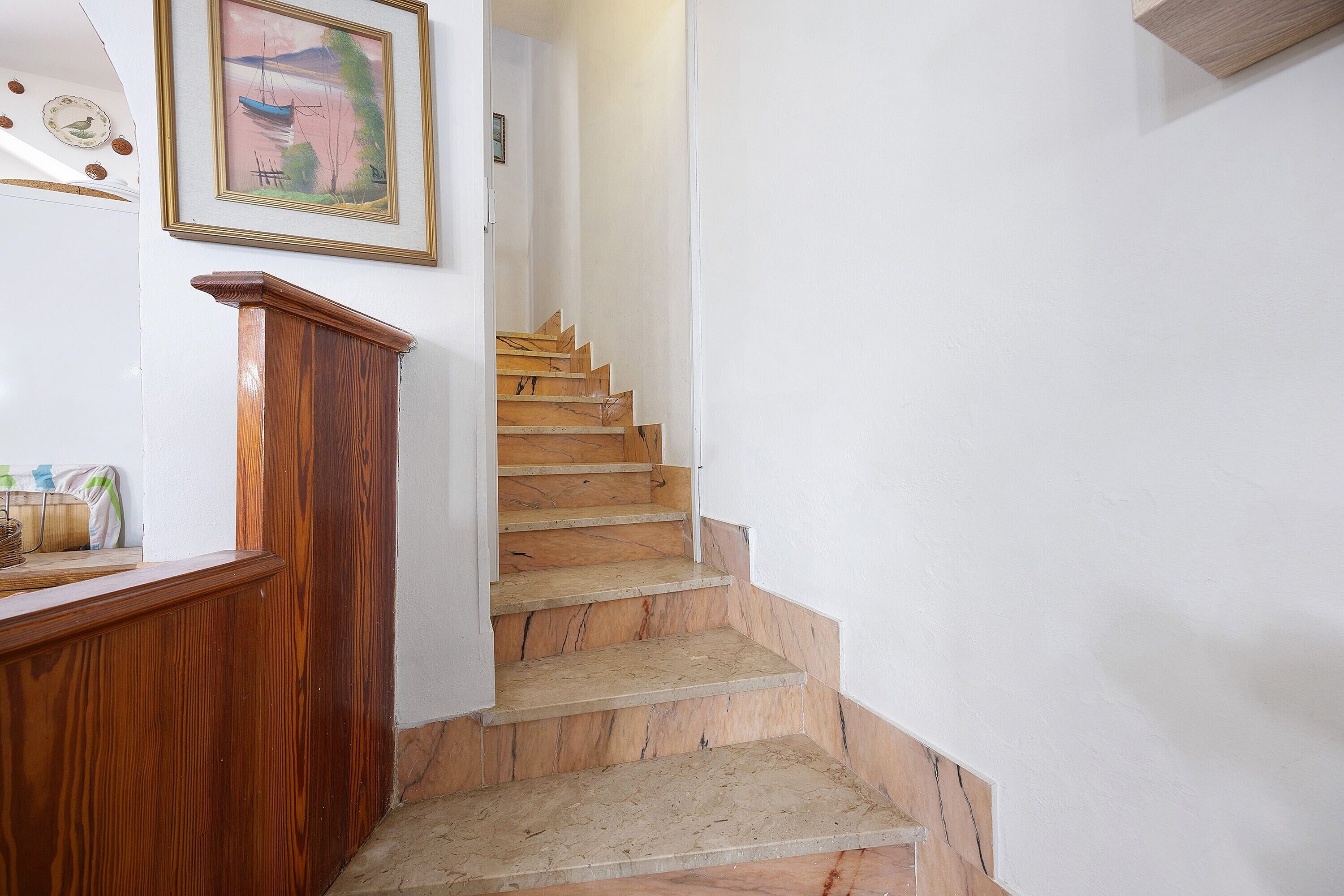 Un escalier avec des marches en bois et une rampe en bois, menant à une pièce dont un mur est blanc et qui contient un tableau encadré.