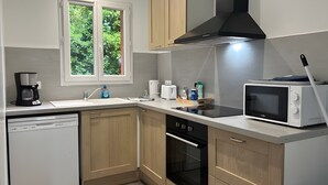 Cozinha moderna com máquina de lavar louça, forno, micro-ondas e janela com vista para o verde.