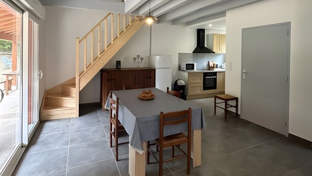Cozinha moderna com área de refeições, escada de madeira e vista através de uma porta de vidro.
