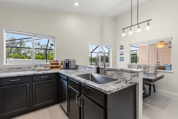 A modern kitchen with dark cabinets, a granite countertop, and a large island with a sink. - Private 3BD2BA Dream Pool Escape Close To Parks (Davenport)