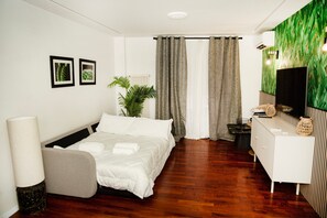 Ein modernes Hotelzimmer mit Bett, Schreibtisch, Pflanze und Wand-Fernseher.