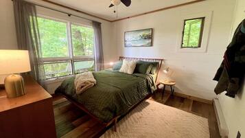 Un dormitorio con cama, escritorio, silla, lámpara, ventilador de techo y ventana.