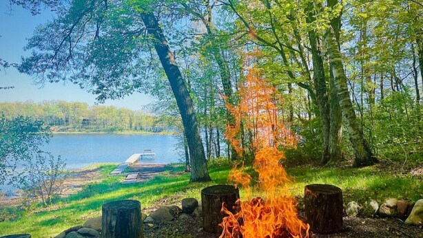 Foc de campament envoltat d'arbres, un moll i un llac.