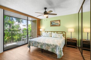Ein Schlafzimmer mit einem Bett, zwei Nachttischlampen, einem Deckenventilator, einem großen Fenster mit Blick auf Grünflächen und einem Bild an der Wand.