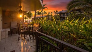 A terrace with chairs and a table, overlooking a sunset with palm trees. - Kona Makai 3-102 No Stairs, Ocean View, With AC! (Kailua-Kona)