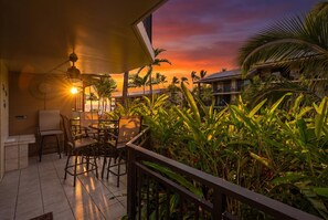 Eine Terrasse mit Stühlen und einem Tisch mit Blick auf einen Sonnenuntergang und Palmen.