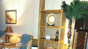 Une pièce comprenant un fauteuil en osier, une armoire en bois avec un miroir, une plante en pot et un tableau accroché au mur.