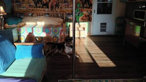Une pièce comprenant un lit, un canapé, un chien, une fresque murale et une porte donnant sur la cuisine.