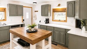 Una cocina con gabinetes grises, una mesa de madera, una cafetera y un ventanal con vistas.