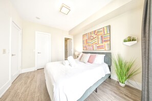 Ein Schlafzimmer mit einem Bett, einem Wandbild, einer Zimmerpflanze und einer Tür.