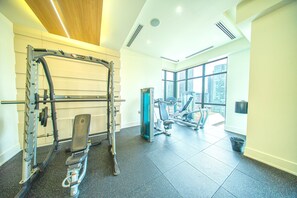 Ein Fitnessraum mit Gewichthebern, einer Bank und einem Fenster mit Blick auf die Stadt.