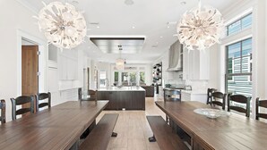 Een moderne keuken met een centraal eiland, houten eettafels en grote hanglampen.