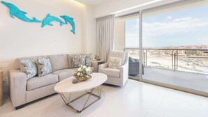 A modern living room with a sofa, armchair, and coffee table, a large window with a city view, and decorative dolphin wall art. - Brand New Sonoran Star Luxury Oceanfront Studio (Puerto Peñasco)