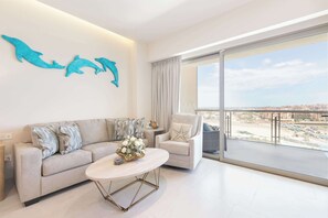 Ein modernes Wohnzimmer mit Sofa, Sessel und Couchtisch, ein großes Fenster mit Blick auf die Stadt und dekorativer Wandgestaltung mit Delphinen.