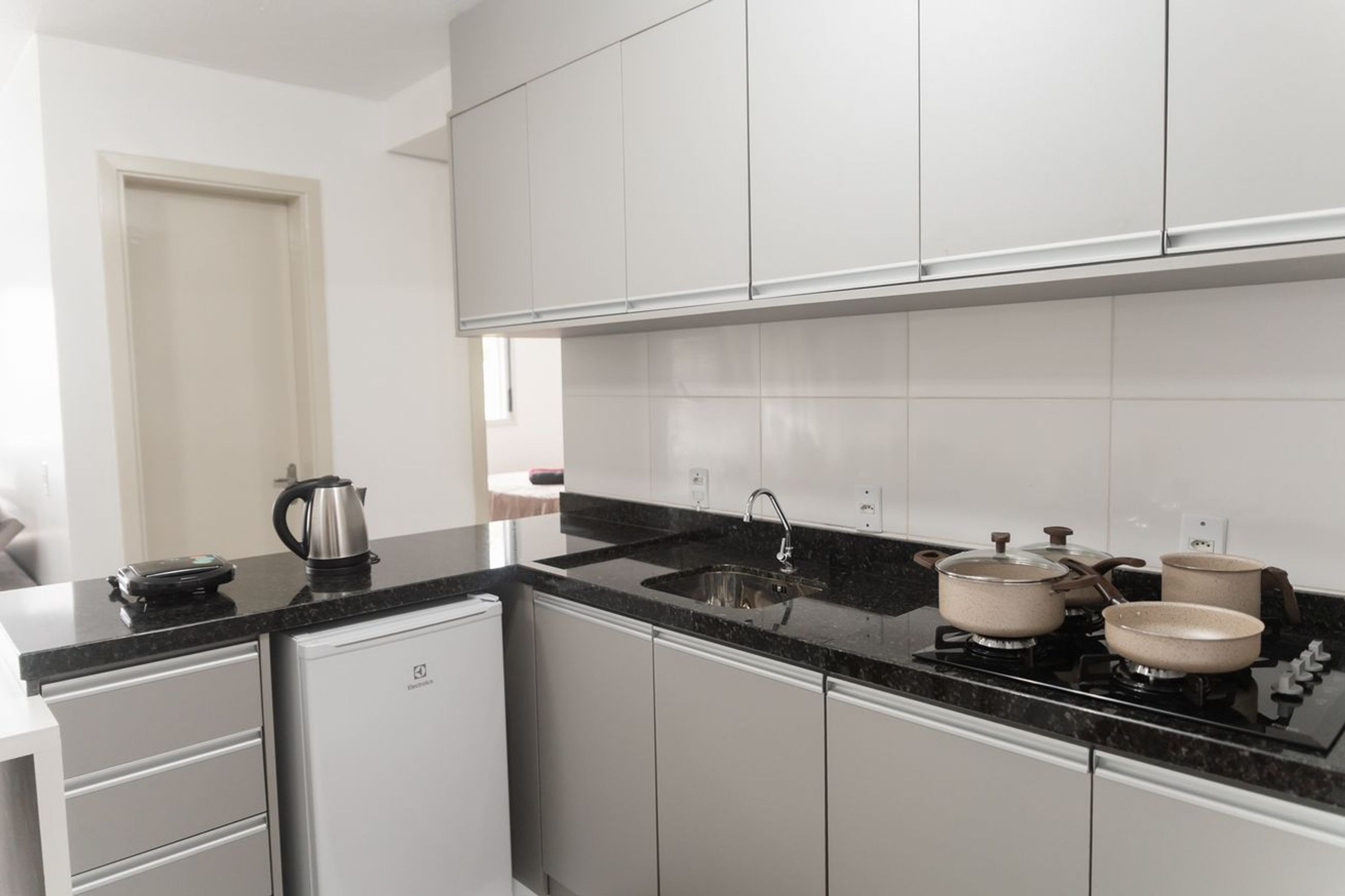 A modern kitchen with white cabinets, a black countertop, and a compact refrigerator.