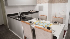 A compact kitchen with a black countertop, white cabinets, a small island with seating, and a tiled backsplash.