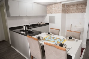 Uma cozinha compacta com bancada preta, armários brancos, uma pequena ilha com assentos e painel de azulejos.