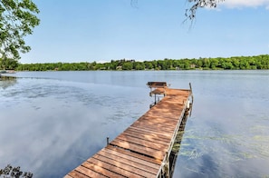 Une jetée en bois s’étendant sur une étendue d’eau calme, entourée d’arbres et bordée par une rive lointaine.