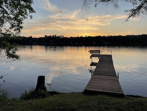 Une jetée en bois s’étendant dans une eau calme, un banc à son extrémité et une rangée d’arbres en arrière-plan.