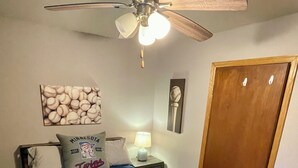 A bedroom with a bed, a ceiling fan, a nightstand with a lamp, a door, and wall decorations. - 2 bedroom walkout on Rice Lake/Mississippi River with dock for your boat! (Brainerd)