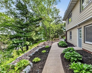 A pathway leading to a house with a garden, trees, and a bench.