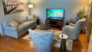 A living room with a sofa, two armchairs, a coffee table, a TV, a lamp, and a painting on the wall. - 2 bedroom walkout on Rice Lake/Mississippi River with dock for your boat! (Brainerd)