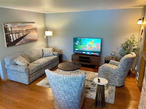 Un salon comprenant un canapé, deux fauteuils, une table basse, un téléviseur, une lampe et un tableau accroché au mur.