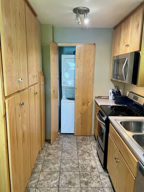 A kitchen with wooden cabinets, a washing machine, a microwave, and a stove.