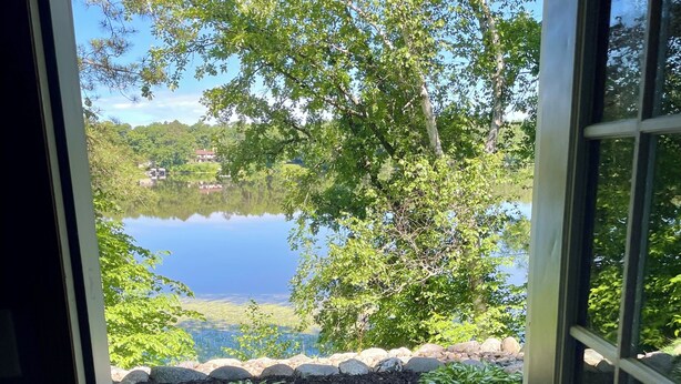 A view through a door to a garden with a stone pathway, a small rug, and a lake with trees. - 2 bedroom walkout on Rice Lake/Mississippi River with dock for your boat! (Brainerd)