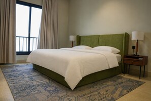 Ein Hotelzimmer mit einem Bett, zwei Nachttischen, einem fenster mit Vorhängen und einem gemusterten Teppich.