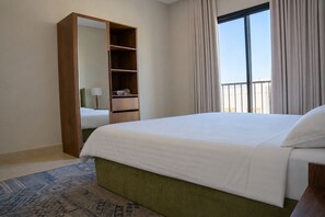 Ein Hotelzimmer mit einem großen Bett, einem Kleiderschrank, einem Balkon mit Vorhängen und einem gemusterten Teppich.