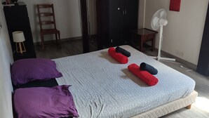 Quarto com cama, almofadas, ventilador, cadeira e guarda-roupa.