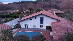 Uma casa com piscina, rodeada por árvores e colinas.