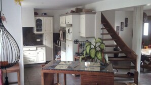 Uma cozinha espaçosa com armários brancos, uma mesa de jantar de madeira e uma escada que leva a outro andar.
