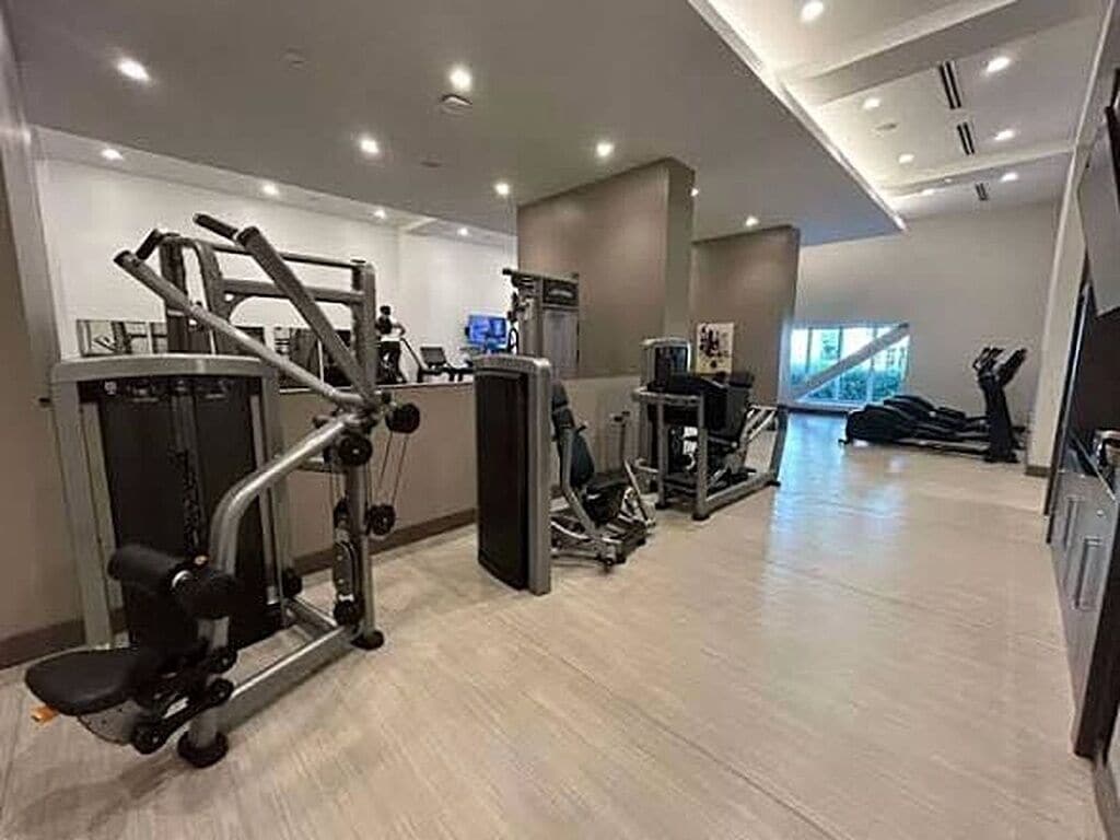Ett gym med olika träningsmaskiner, en stor spegel och ett fönster med utsikt över omgivningen.