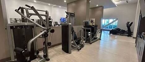 Ett gym med olika träningsmaskiner, en stor spegel och ett fönster med utsikt över omgivningen.