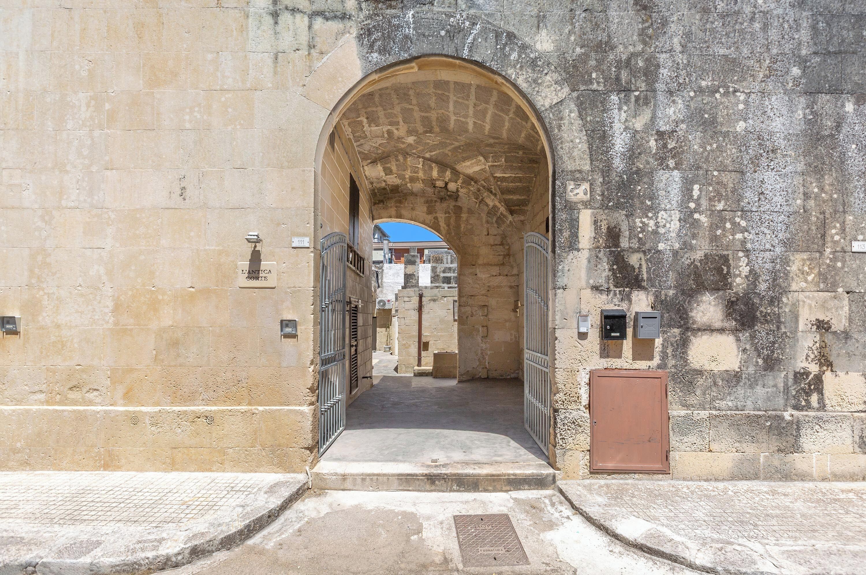 An arched entrance to a building with a metal gate, a small step leading up to it, and a brown door to the right.
