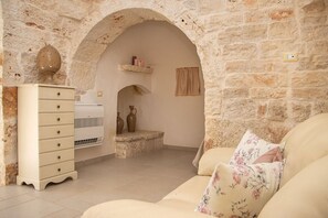 Ein Zimmer mit einer Steinsäule, einem weißen Schminktisch, einem beigen Sofa und einem kleinen Tisch mit zwei Vasen.