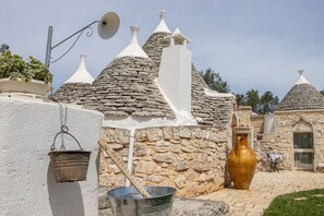 A traditional stone building with conical roofs, a large ceramic vase, and a metal bucket. - Trullo Canicchiulo by BarbarHouse (Latiano)