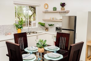 A modern kitchen with a dining table set for four, a refrigerator, and a window with a view of trees. - Ecovillas del Sur (San Juan del Sur)