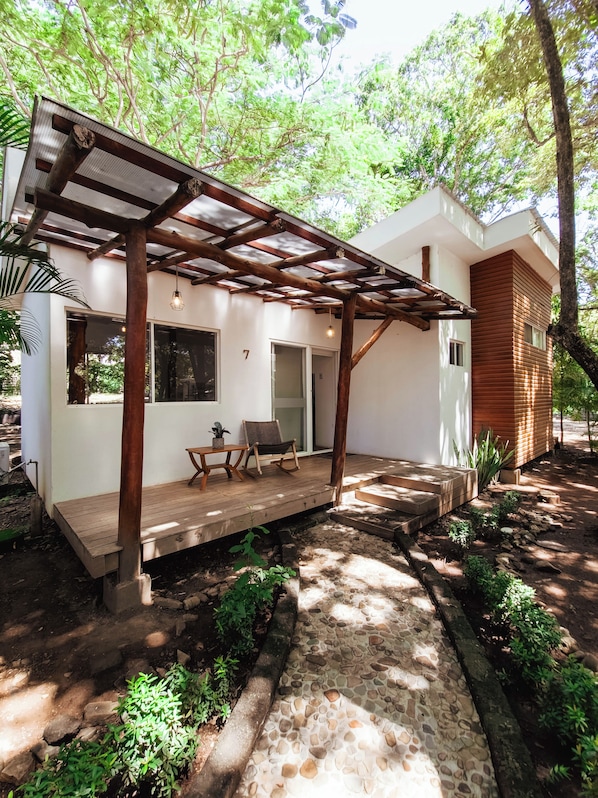 Un espacio al aire libre cubierto con terraza de madera, un conjunto de asientos y una escalera que lleva a un edificio.