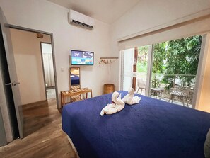 Habitación de hotel con cama, televisión, una mesita y ventana con vistas a zonas verdes.