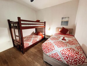 Una habitación con dos literas, una mesita de noche con lámpara y una obra de arte colgada en la pared.
