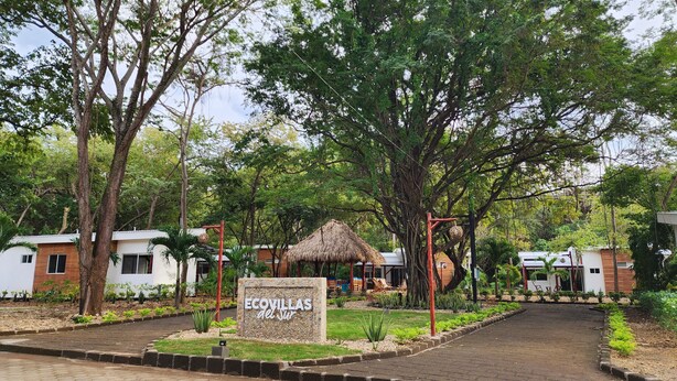 Ein Resort mit strohgedeckten Hütten, einem Schild mit der Aufschrift 'ECOVILLAS de Sur' und einem gepflasterten Weg, der zu den Gebäuden führt.