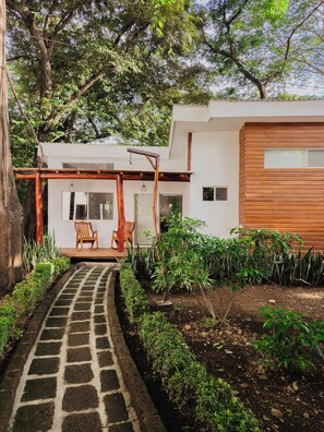 Una casa moderna con un camino empedrado que lleva a un porche de madera con sillas.